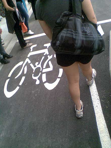 People stand in the bike lane while waiting for the traffic lights